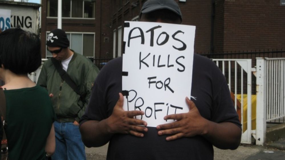 Un manifestant anglais, se cachant le visage avec un panneau o&ugrave; est &eacute;crit &quot;Atos kill for profits&quot; (Atos tue pour des profits).